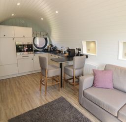 An open plan living room and kitchen with two chairs at a breakfast bar and a sofa with a cushion at The Hazel Pod in Cowbridge