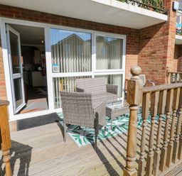 A small outdoor seating area with two wicker chairs and a glass-top table on a wooden deck at 98 Waterside Park in Corton