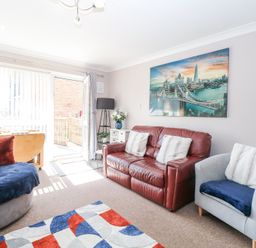 A living room with a red leather sofa a gray armchair and a colorful rug at 98 Waterside Park in Corton