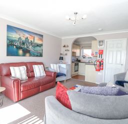 A living room with a red leather sofa, three armchairs, a small round table, and an open kitchen at 98 Waterside Park in Corton