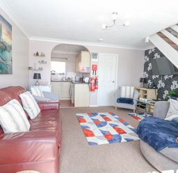 A living room with a red leather sofa, two armchairs, a patterned rug, a wall-mounted TV, and a view into a kitchen at 98 Waterside Park in Corton
