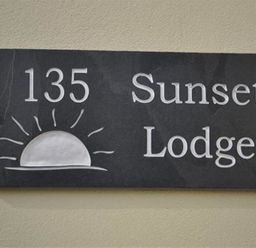 A black rectangular sign with the number 135 a sunrise illustration and the words Sunset Lodge
