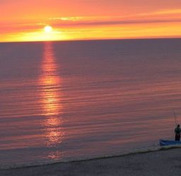 A person fishing on a beach at sunset over calm sea at Sunset Lodge in Fortuneswell