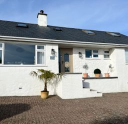 The exterior of a white house with potted plants near the entrance at Trem Ynys 3 bed in Abersoch