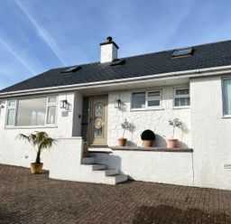 The exterior front of a white house with steps leading to a beige door and potted plants on the porch at Trem Ynys 3 bed in Abersoch