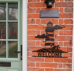 A green door next to a brick wall with a lighthouse welcome sign and a house number plaque at 1 Rumsby Cottages Gisleham near Kessingland