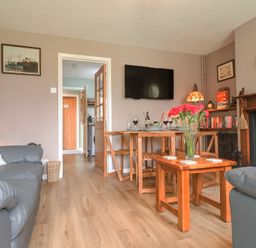 A living room with wooden tables a television and a fireplace at 1 Rumsby Cottages in Gisleham near Kessingland