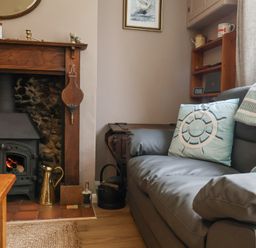 A living room with a wood burning stove fireplace a gray sofa with blue cushions and a wooden side table at 1 Rumsby Cottages Gisleham near Kessingland