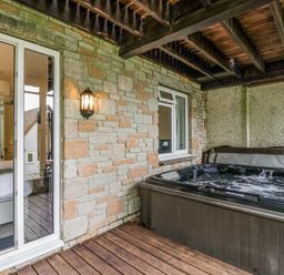 A covered outdoor area with a hot tub next to a stone wall and a door leading to a bedroom at 23 Valley Lodge in Gunnislake