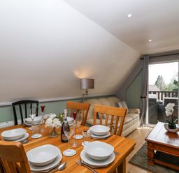 A dining table set with plates glasses and cutlery next to a beige sofa and a wooden coffee table with a plant by sliding glass doors at 23 Valley Lodge in Gunnislake