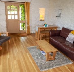 A sitting room with wooden table and chairs a brown leather sofa and a door with windows at Babes Cottage in Perranwell near Goonhavern