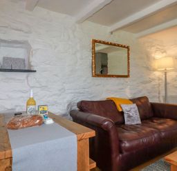 A living room with a brown leather sofa a wooden table with bread a bottle and a carton and a floor lamp at Babes Cottage in Perranwell near Goonhavern