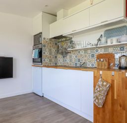 A kitchen with white cabinets wooden countertops patterned tile backsplash and a wall mounted TV at The Lookout in Perranwell near Goonhavern