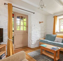 A sitting room with a blue sofa wooden coffee table and television at Hollies Cottage Perranwell near Goonhavern