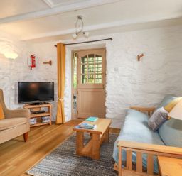 A living room with a sofa a chair a coffee table a wooden door and a television at Hollies Cottage Perranwell near Goonhavern