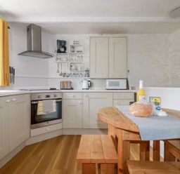 A kitchen with wooden floor cabinets a wooden table with bench seating and kitchen appliances at Hollies Cottage in Perranwell near Goonhavern