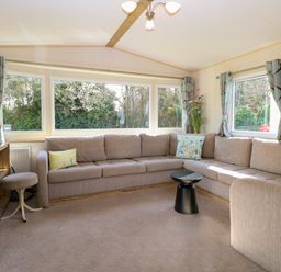 A living room with a large beige sectional sofa and small black round table at 4 Foxburrow Hang in Fritton near Belton Norfolk