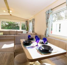 A dining area with a table set with blue glasses and black plates beside a window with patterned curtains and a living room with a beige sofa at 4 Foxburrow Hang in Fritton near Belton Norfolk
