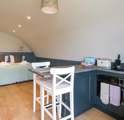 A bedroom with a bed and pillows near a kitchen with a countertop and two white chairs at Creags Cullipool Isle Of Luing