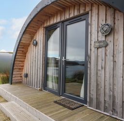 A wooden cabin with glass double doors and a small porch at Erraid South Cuan near Cullipool Isle Of Luing