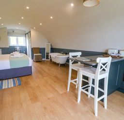 A studio room with a bed towels a bathtub chairs a small kitchen area and a window at Erraid in South Cuan near Cullipool Isle Of Luing