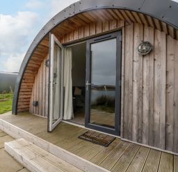 The exterior of a wooden cabin with an arched roof and open glass doors at Insh Cullipool Isle Of Luing