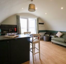 A living area with a kitchen counter, two white chairs, a green sofa, two round woven chairs, and double doors leading outside at Insh Cullipool Isle Of Luing