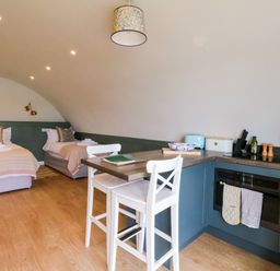 A room with two single beds and a kitchen area with a breakfast bar and two white stools at Insh Cullipool Isle Of Luing
