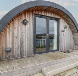 A wooden curved front entrance with glass double doors and steps at Sula in Cullipool Isle Of Luing