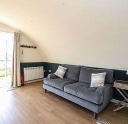 A living room with a gray sofa two pillows a wooden side table with a lamp a curtain a coat rack and a glass door at Scarba in Cullipool Isle Of Luing