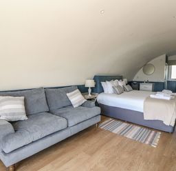 A bedroom with a gray sofa, bed with pillows and folded towels, a small side table with lamp and a window at Scarba Cullipool Isle Of Luing