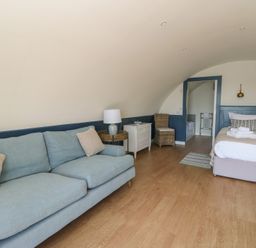A bedroom with a blue sofa white nightstand bed and wooden floor at Torsa Cullipool Isle Of Luing