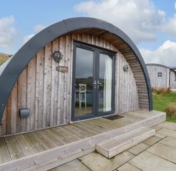 A wooden cabin with curved roof and glass double doors on a stone and wooden deck at Fladda in Cullipool Isle Of Luing