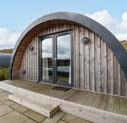 A wooden arched cabin with double glass doors and a small step outside at Fladda in Cullipool Isle Of Luing