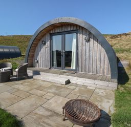 A wooden curved cabin with glass doors a patio with chairs and a fire pit at Losal Cullipool Isle Of Luing