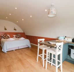 A room with a double bed with patterned cushions and folded towels a kitchen counter with two chairs and kitchen appliances at Losal in Cullipool Isle Of Luing