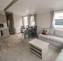 A living room with a sofa a coffee table a dining table with chairs and a kitchen area at Meadow View in West Thirston Felton