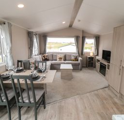 A living area with a dining table set with plates and glasses a sofa with cushions a coffee table a television on a cabinet and windows with curtains at Meadow View in West Thirston Felton