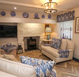 A sitting room with cream sofas blue patterned cushions a stone fireplace and a wall-mounted television at 6 Uppergate Street Rose Cottage in Conwy