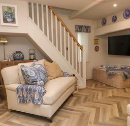 A living room with a beige sofa under stairs and a mounted TV surrounded by decorative plates at 6 Uppergate Street Rose Cottage in Conwy