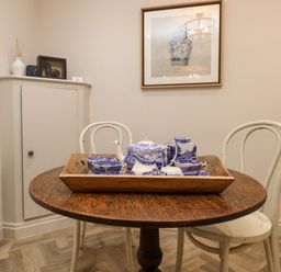 A wooden round table with a tray holding blue and white tea set and two white chairs in a dining area at 6 Uppergate Street Rose Cottage in Conwy