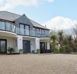 The exterior of a two story house with a paved driveway and glass balcony at Goatsland in Trebetherick