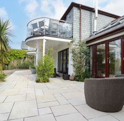 Outdoor patio area with wicker chairs plants and balconies with glass railings at Goatsland in Trebetherick