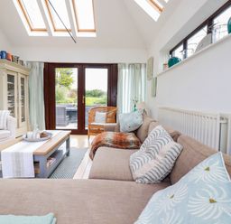 A living room with a sofa and armchair around a coffee table under skylights at Goatsland in Trebetherick