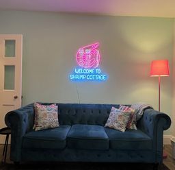 A living room with a blue sofa and a neon sign at Shrimp Cottage in Brewers Quay Harbour