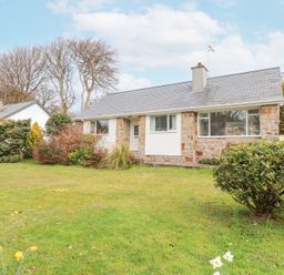 A front view of a stone and white house with a lawn and bushes at 3 Glyn Y Mor in Llanbedrog