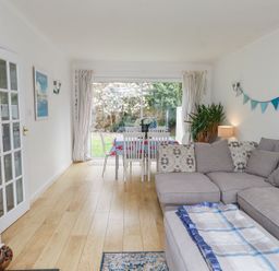 A living room with a gray sectional sofa and a dining table with white chairs near a sliding glass door at 3 Glyn Y Mor in Llanbedrog