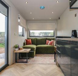 A small living area with a green sofa and two side tables next to a kitchen unit at Caban in Dothan near Gwalchmai