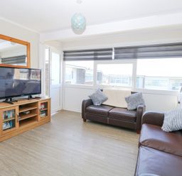 A living room with two brown leather sofas next to windows with blinds and a television on a wooden stand with a mirror above at Chalet 38 in Hemsby