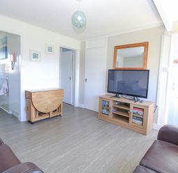 A living room with two brown sofas a wooden TV stand with a television and a wooden folding table near the kitchen at Chalet 38 in Hemsby